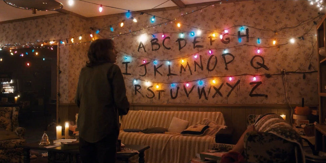 Joyce devant le mur de l'alphabet et ses guirlandes allumées dans Stranger Things