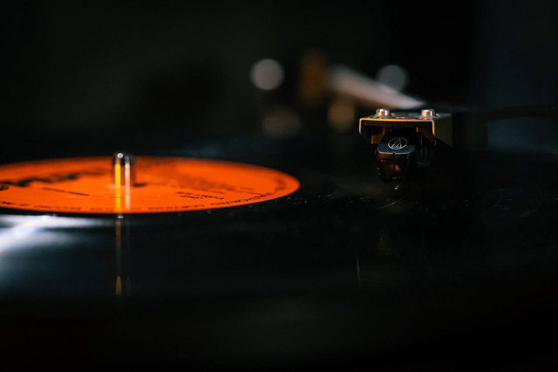 Un vinyle tourne sur la platine, bras de lecture posé sur le sillon, reflets orangés dans la pénombre