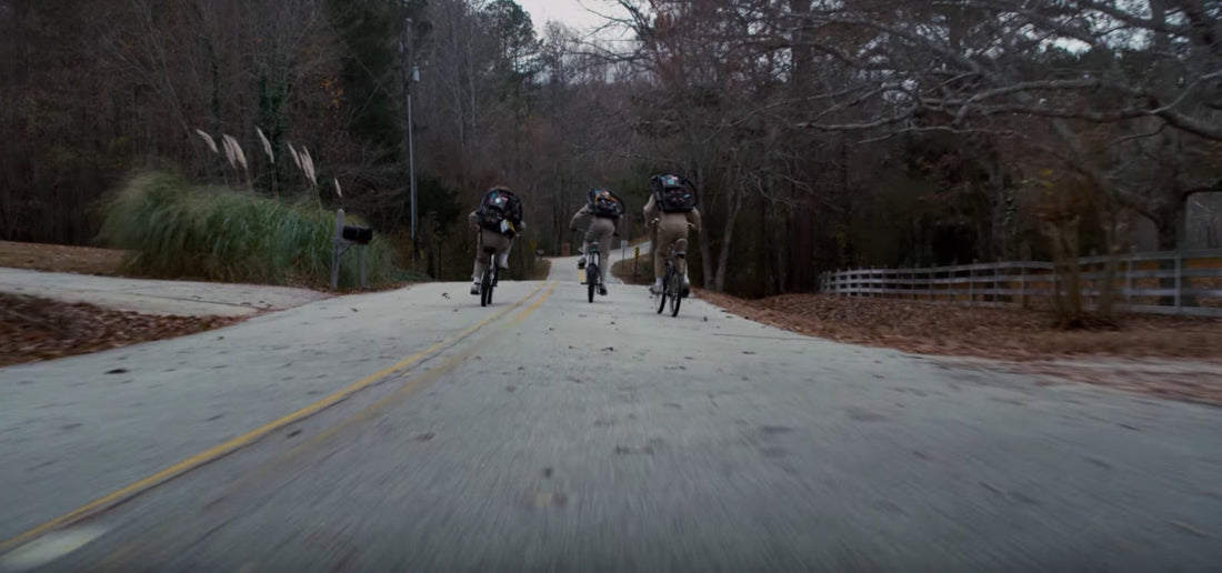 Trois cyclistes vus de dos, sacs au dos, sur une route bordée d'arbres