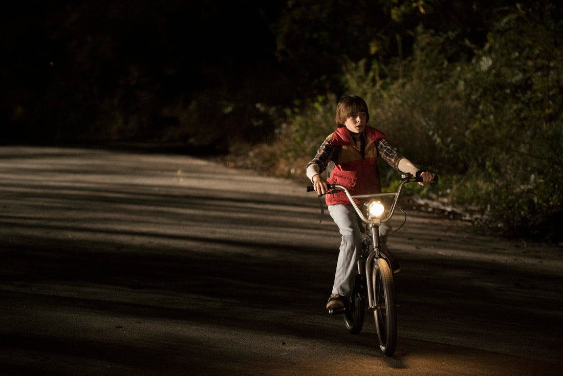 Will à vélo, la nuit, sur une route bordée d'arbres, le phare allumé.